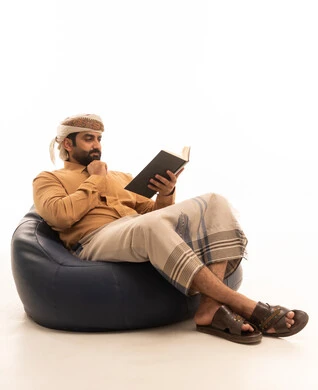 قضاء وقت الفراغ بالتعلم والثقافة، مفهوم التثقيف والبحث العلمي، هواية المطالعة والاستكشاف، بورتريه لرجل عربي يمني يرتدي القميص والازار مع العمامة يجلس على كرسي بين باج يمسك كتاب ويضع يده على ذقنه بتعابير التفكير، خلفية بيضاء