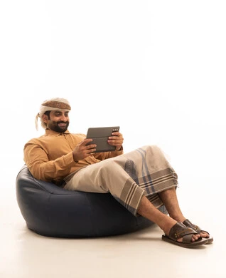 المحادثة مع الأهل والأصدقاء، استعمال التكنولوجيا والتقنية الحديثة, تصفح مواقع التواصل الاجتماعي عبر الجهاز اللوحي، بورتريه لرجل عربي يمني يرتدي القميص والازار مع العمامة يجلس على كرسي بين باج يحمل بيده جهاز التابلت، خلفية بيضاء