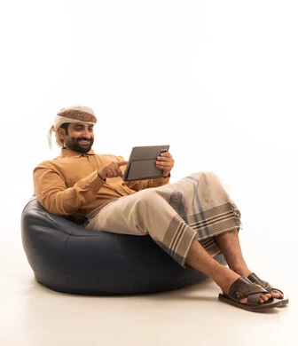 استعمال التكنولوجيا والتقنية الحديثة, تصفح مواقع التواصل الاجتماعي عبر الجهاز اللوحي، المحادثة مع الأهل والأصدقاء، بورتريه لرجل عربي يمني يرتدي القميص والازار مع العمامة يجلس على كرسي بين باج يحمل بيده جهاز التابلت، خلفية بيضاء