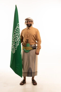 إيماءات الفخر و السرور بالانتماء للوطن، إحياء ذكرى اليوم الوطني السعودي 23 سبتمبر، يوم العلم السعودي 11 مارس, بورتريه لرجل عربي يمني يرتدي القميص والازار مع العمامة والجنبية يحمل بيده علم المملكة، يوم بدينا 1727 م، الجسم بالطول الكامل، خلفية بيضاء
