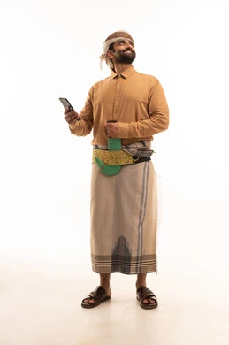النظر الى شي ما، استخدام التقنيات والتكنولوجيا الحديثة بالحياة اليومية، الدردشة والتحدث مع الأصدقاء،تصفح مواقع وتطبيقات الانترنت، بورتريه لرجل عربي يمني يرتدي القميص والازار مع العمامة والجنبية يمسك الجوال بيده، الجسم بالطول الكامل، خلفية بيضاء