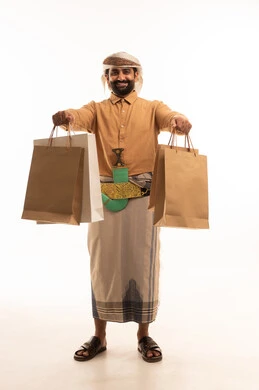 Buying new items and supplies, enjoying shopping and taking advantage of offers. Portrait of a Yemeni Arab man wearing a shirt and izar with a turban and jambiya, holding paper bags in his hands. Full-length body, white background.