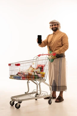 عرض شاشة سوداء فارغه عبر الجوال، الاستفادة من الخصومات والتنزيلات، بورتريه لرجل عربي يمني يرتدي القميص والازار مع العمامة والجنبية يمسك الهاتف المحمول بيده و عربة المشتريات بإيماءات السرور، خلفية بيضاء