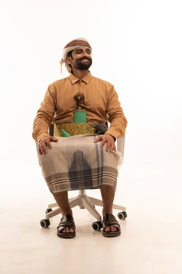 المحافظة على اللباس التقليدي، تمثيل الرجولة العربية الأصيلة، النظر الى شيء ما بتعابير السعادة و السرور، بورتريه لرجل عربي يمني يرتدي القميص والازار مع العمامة والجنبية يجلس على كرسي، خلفية بيضاء