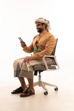 تمثيل الرجولة العربية الأصيلة، بورتريه لرجل عربي يمني يرتدي القميص والازار مع العمامة والجنبية يجلس على كرسي يحمل الهاتف المحمول، تبادل الأحاديث و الأخبار الجيدة، إيماءات السعادة بالتواصل مع الأصدقاء والأقارب، المحافظة على اللباس التقليدي