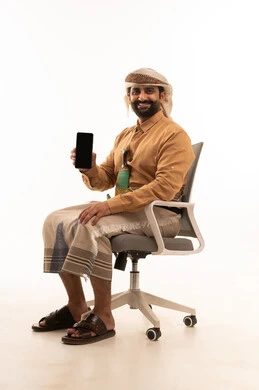 A black screen displayed on the mobile phone, expressions of happiness and joy, a portrait of a Yemeni Arab man wearing a shirt and a sarong with a turban and a jambiya sitting on a chair holding a mobile phone in his hands, white background.