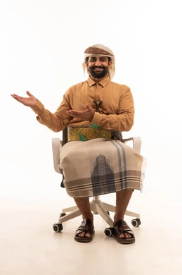 Expressions of happiness and joy, pointing to the palm of the hand, presenting and displaying an item, lifting and carrying items, a portrait of a Yemeni Arab man wearing a shirt and izar with a turban and jambiya sitting on a chair raising his hand forward with gestures of carrying something, white background.