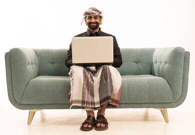 تصفح الانترنت ووسائل التواصل الاجتماعي، انجاز الاعمال والمهام عن بعد عبر الحاسوب المحمول، بورتريه لرجل عربي يمني يرتدي القميص والازار مع العمامة يقوم باستخدام الحاسب، خلفية بيضاء