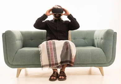 المتعة و التسلية بالمشاهدة عبر نظارة الواقع الافتراضي،الاندماج ومحاكاة العالم الخيالي والنظر الى الافلام الواقعيه، التطور التقني والتكنولوجي، بورتريه لرجل عربي يمني يرتدي القميص والازار مع العمامة يجلس على الاريكة ينظر من خلال نظارات ثلاثية الأبعاد (الفي ار)، خلفيه بيضاء