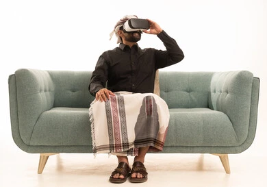 الاندماج ومحاكاة العالم الخيالي والنظر الى الافلام الواقعيه، التطور التقني والتكنولوجي, المتعة و التسلية بالمشاهدة عبر نظارة الواقع الافتراضي، بورتريه لرجل عربي يمني يرتدي القميص والازار مع العمامة يجلس على الاريكة ينظر من خلال نظارات ثلاثية الأبعاد (الفي ار)، خلفيه بيضاء