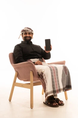 عرض شاشة سوداء فارغة عبر اللابتوب، العمل عن بعد، تصفح مواقع التواصل الإجتماعي، استخدام جهاز تقني حديث ومتطور لانجاز المشاريع، بورتريه لرجل عربي يمني يرتدي القميص والازار مع العمامة يجلس على كرسي يستخدم الحاسوب المحمول، خلفية بيضاء