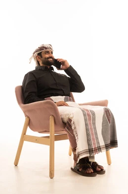 تبادل الأحاديث و الأخبار الجيدة، إجراء مكالمة هاتفية صوتية عبر الجوال، بورتريه لرجل عربي يمني يرتدي القميص والازار مع العمامة يجلس على كرسي يتحدث عبر الهاتف المحمول، إيماءات السعادة بالتواصل مع الأصدقاء والأقارب, خلفية بيضاء