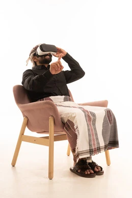 الاشارة الي شيء ما, ارتداء نظارة الفي آر ثلاثية الأبعاد, التطور التقني والتكنولوجي ,بورتريه لرجل عربي يمني يرتدي القميص والازار مع العمامة يجلس على كرسي ينظر من خلال نظارات الواقع الافتراضى, إيماءات الاندماج ومحاكاة العالم الخيالي، خلفية بيضاء