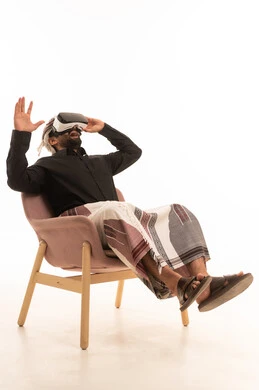 Wearing 3D VR glasses, technological and technical evolution, a portrait of a Yemeni Arab man wearing a shirt and a waist wrap with a turban sitting on a chair looking through virtual reality glasses, gestures of immersion and simulation of the imaginary world, white background.
