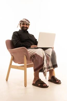 تصفح الانترنت وبرامج التواصل الاجتماعي، استخدام الحاسب المحمول في انجاز المهام, بورتريه لرجل عربي يمني يرتدي القميص والازار مع العمامة يجلس على كرسي يمسك بيدية الابتوب, تطور الاجهزة والتقينات الحديثة, خلفية بيضاء
