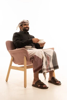 النظر الى شيء ما، تأثير الكافيين على نشاط الدماغ والذاكرة، الاستمتاع بتناول المشروبات الساخنة والأعشاب الشتوية الدافئة، بورتريه لرجل عربي يمني يرتدي القميص والازار مع العمامة يجلس على كرسي يحمل بيده كوب من القهوة، خلفية بيضاء