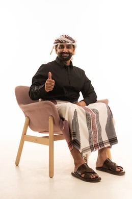 Gestures of acceptance, joy, and happiness, attention to elegance and appearance, a portrait of a Yemeni Arab man wearing a shirt and a sarong with a turban sitting on a chair looking at the camera raising his index finger upwards with expressions of admiration and satisfaction, white background.