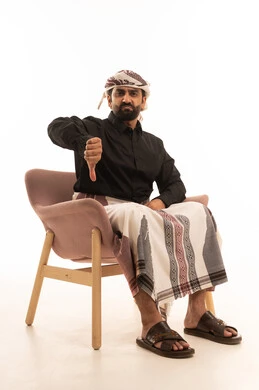 مفهوم الرفض وعدم القبول،بورتريه لرجل عربي يمني يرتدي القميص والازار مع العمامة يجلس على كرسي يشير بإصبع الابهام للاسفل بإيماءات عدم الاعجاب والتقييم السلبي، الشعور بالانزعاج من شيء ما, خلفية بيضاء