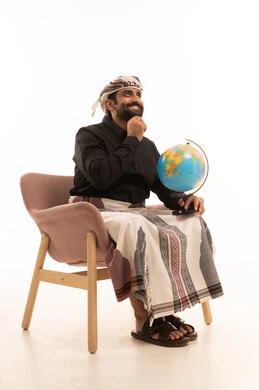 النظر الى شيء ما، التعرف على جغرافيا البلاد، حب البحث والاستكشاف، تمييز الحدود البرية والبحرية للدول، بورتريه لرجل عربي يمني يرتدي القميص والازار مع العمامة يجلس على كرسي يحمل بيده مجسم مصغر للكرة الأرضية و يضع يدية على ذقنة بإيماءات السعادة و السرور, خلفية بيضاء