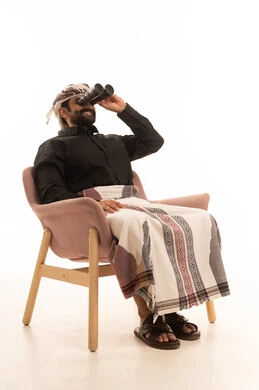 Gestures of happiness and joy, seeing distant things through a telescope, a love for adventure and exploration, a forward-looking perspective, a portrait of an Arab Yemeni man wearing a shirt and a waist wrap with a turban sitting on a chair and looking through a binocular, white background.