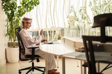 اجراء بث مباشر ، استخدام الحاسب و التقنية في مجال الاعمال، مفهوم التركيز و الدقة في الإنجاز، مهنة و وظيفة عمانية مكتبية, إتمام مهام العمل في المكتب، موظف عربي خليجي عماني يرتدي الدشداشة والكمة ويقوم باستخدام اللابتوب