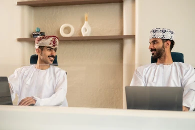 العمل الجماعي و التعاون، الاستعانة بالأجهزة التقنية الحديثة، إتمام المهام في المكتب، تطور الشركات العمانية ,موظفان عربيان خليجيان عمانيان يرتديان الدشداشة والكمة عمانيان ويقومان باستخدام اللابتوب و التابلت, الجلوس على كرسي مريح