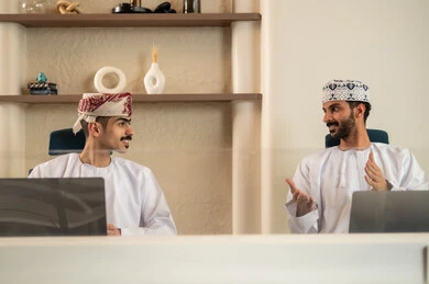 الاستعانة بالأجهزة التقنية الحديثة، إتمام المهام في المكتب، تطور الشركات العمانية , العمل الجماعي و التعاون، موظفان عربيان خليجيان عمانيان يرتديان الدشداشة والكمة عمانيان ويقومان باستخدام اللابتوب و التابلت, الجلوس على كرسي مريح