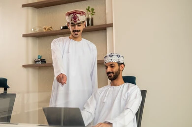 شرح واضح للتاسكات , نقاش و حوار في بيئة مكتبية, تقسيم المهام بين الموظفين, متابعة المهام اليومية، إنجاز الأعمال المكتبية، مفهوم ادارة المشاريع، تطوير الخطط وتحقيق أهداف الشركة، فريق عمل عربي خليجي عماني يجلسون على مكتب يستخدمون الحاسوب المحمول