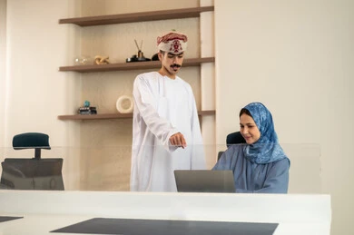 Completion of office work, the concept of project management, a clear explanation of tasks, discussion and dialogue in an office environment, division of tasks among employees, monitoring daily tasks, developing plans and achieving the company's goals, an Arab Gulf Omani team sitting at a desk using a laptop.