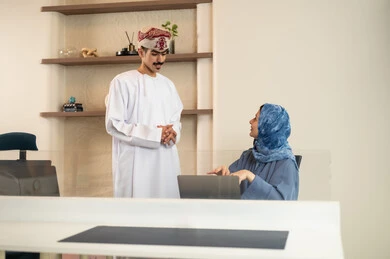 A clear explanation of tasks, discussion and dialogue in an office environment, division of tasks among employees, follow-up on daily tasks, completion of office work, the concept of project management, developing plans and achieving the company's goals, an Arab Gulf Omani team sitting at a desk using a laptop.