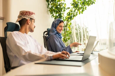 A clear explanation of tasks, discussion and dialogue in an office environment, division of tasks among employees, follow-up on daily tasks, completion of office work, the concept of project management, developing plans and achieving the company's goals, an Arab Gulf Omani team sitting at a desk using a laptop.
