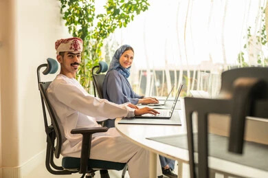 A clear explanation of tasks, discussion and dialogue in an office environment, division of tasks among employees, follow-up on daily tasks, completion of office work, the concept of project management, developing plans and achieving the company's goals, an Arab Gulf Omani team sitting at a desk using a laptop.