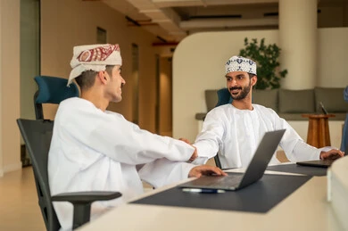 Discussion and dialogue in an office environment, clear explanation of tasks, division of tasks among employees, follow-up on daily tasks, completion of office work, concept of project management, developing plans and achieving company goals, a Gulf Arab Omani team sitting at a desk using a laptop.