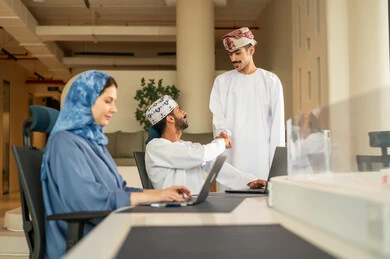 تطوير الخطط وتحقيق أهداف الشركة، صفقات شراكة جديدة، الحوارات و النقاشات حول المشاريع،التعاون و المشاركة في إنجاز الأعمال، فريق عمل عربي خليجي عماني مكون من رجلين يرتديان الدشداشة و الكمة و سيدة محجبة ترتدي عباءة زرقاء, مصافحة و سلام حار بين الزملاء
