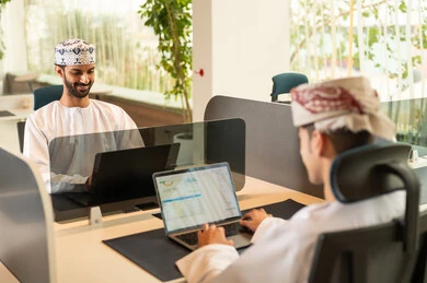 فريق عربي خليجي عماني مكون من رجلين يرتديان الدشداشة والكمة , دمج التقنيات المتطورة فى العمل ،التعاون و متابعة الاعمال, نمط الحياة في الشركات العمانية ، تدريب الموظفين على سياسات العمل لتحقيق الأهداف في المكتب داخل مقر الشركة، انجاز المهام من خلال اللابتوب و التابلت