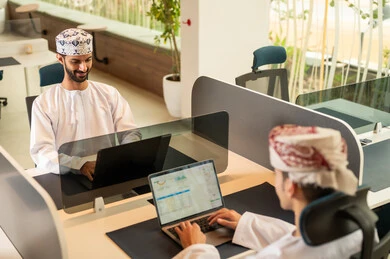 دمج التقنيات المتطورة فى العمل ،التعاون و متابعة الاعمال, نمط الحياة في الشركات العمانية ، تدريب الموظفين على سياسات العمل لتحقيق الأهداف في المكتب داخل مقر الشركة، فريق عربي خليجي عماني مكون من رجلين يرتديان الدشداشة والكمة , انجاز المهام من خلال اللابتوب و التابلت