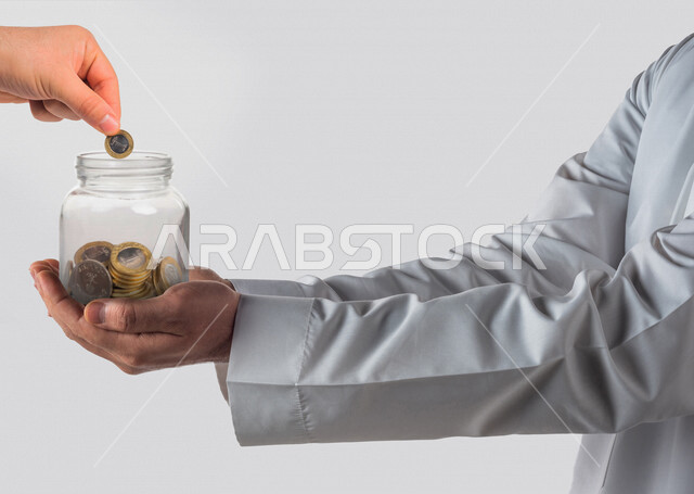 صورة مقربة ليد رجل عربي خليجي سعودي يحمل بين يديه عملات معدنية تعبيرا عن الإدخار ، جمع التبرعات المالية ، الاستثمار و التنمية المالية 