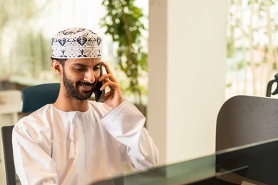 Managing and organizing business affairs via a laptop, pressing the keyboard keys, integrating work with technology and tech, an Arab Gulf Omani man wearing a dishdasha and kumma using a laptop, the concept of completing tasks remotely, a comfortable office work environment.