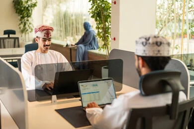 تدريب الموظفين على سياسات العمل لتحقيق الأهداف في المكتب داخل مقر الشركة، نمط الحياة في الشركات العمانية، دمج التقنيات المتطورة فى العمل ،التعاون و متابعة الاعمال,فريق عربي خليجي عماني مكون من رجلين يرتديان الدشداشة والكمة  وسيدة محجبة ترتدي العباءة الزرقاء , انجاز المهام من خلال اللابتوب و التابلت