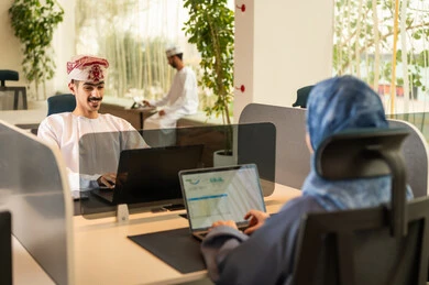 نمط الحياة في الشركات العمانية، تدريب الموظفين على سياسات العمل لتحقيق الأهداف في المكتب داخل مقر الشركة، دمج التقنيات المتطورة فى العمل ،التعاون و متابعة الاعمال,فريق عربي خليجي عماني مكون من رجلين يرتديان الدشداشة والكمة  وسيدة محجبة ترتدي العباءة الزرقاء , انجاز المهام من خلال اللابتوب و التابلت