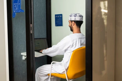 Performing daily tasks inside the company headquarters, gestures of integration and interaction, an Arab Gulf Omani employee wearing a dishdasha and kumma using a laptop, integrating technology and modern devices with practical life.