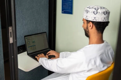 أداء المهمة اليومية داخل مقر الشركة, ايماءات الاندماج والتفاعل, موظف عربي خليجي عماني يرتدي الدشداشة والكمة يقوم باستخدام الحاسوب المحمول , دمج التقنية و الأجهزة الحديثة مع الحياة العملية