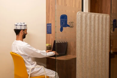 Performing daily tasks inside the company headquarters, gestures of integration and interaction, an Arab Gulf Omani employee wearing a dishdasha and kumma using a laptop, integrating technology and modern devices with practical life.