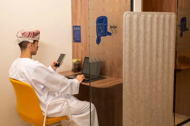 Performing the daily task inside the company headquarters, observing expressions of integration and interaction, an Arab Gulf Omani employee wearing a dishdasha and kumma is using a laptop and holding a mobile phone in his hand, integrating technology and modern devices with practical life.