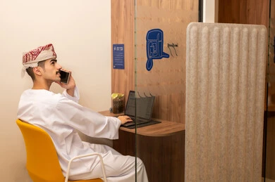 أداء المهمة اليومية داخل مقر الشركة, النظر بتعبيرات الاندماج والتفاعل, موظف عربي خليجي عماني يرتدي الدشداشة والكمة يقوم باستخدام الحاسوب المحمول ويحمل بيده الهاتف المحمول , دمج التقنية و الأجهزة الحديثة مع الحياة العملية