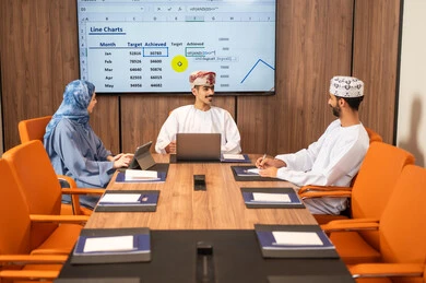 شرح و تحليل الرسوم البيانية, استخدام الحاسوب المحمول ،إدارة و تقسيم المهام، فريق عمل عربي خليجي عماني يقوم بإجراء اجتماع عمل داخل غرفة الاجتماعات في مقر الشركة، دمج الأجهزة التقنية الحديثة بالأعمال المكتبية، دراسة أوراق البيانات الإحصائية, تطوير المشاريع و الاستثمارات