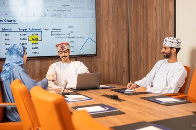 Management and task division, a Gulf Arab Omani team conducting a business meeting inside the conference room at the company's headquarters, explaining and analyzing charts, using a laptop, integrating modern technological devices with office work, studying statistical data sheets, developing projects and investments. Management and task division, a Gulf Arab Omani team conducting a business meeting inside the conference room at the company's headquarters, explaining and analyzing charts, using a laptop, integrating modern technological devices with office work, studying statistical data sheets, developing projects and investments.
