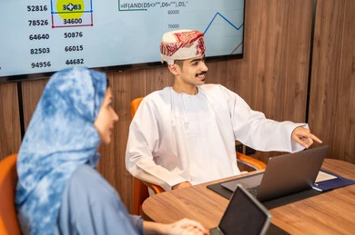 دمج الأجهزة التقنية الحديثة بالأعمال المكتبية، إدارة و تقسيم المهام، فريق عمل عربي خليجي عماني يقوم بإجراء اجتماع عمل داخل غرفة الاجتماعات في مقر الشركة، شرح و تحليل الرسوم البيانية, استخدام الحاسوب المحمول ، تطوير المشاريع و الاستثمارات
