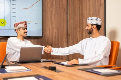 Management and task division, a Gulf Arab Omani team conducting a business meeting inside the conference room at the company's headquarters, explaining and analyzing charts, using a laptop, integrating modern technological devices with office work, studying statistical data sheets, developing projects and investments.