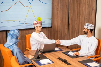 Management and task division, a Gulf Arab Omani team conducting a business meeting inside the conference room at the company's headquarters, explaining and analyzing charts, using a laptop, integrating modern technological devices with office work, studying statistical data sheets, developing projects and investments.